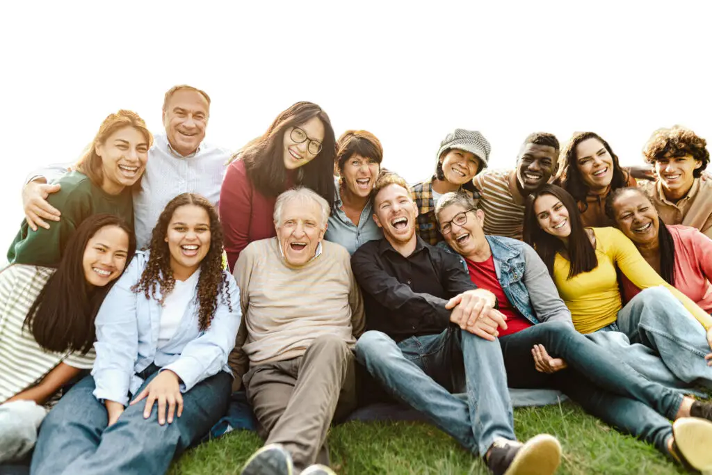 Happy multigenerational people having fun sitting on grass in a public park