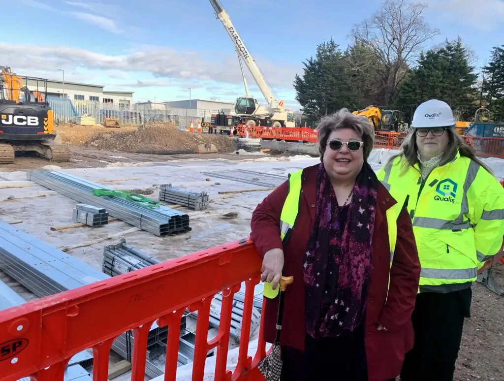 Two women in high visibility vests on a construction site smiling at camera